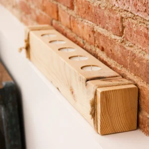 Portavelas de madera para 5 velas Poloka sobre una repisa, con pared de ladrillo visto al fondo