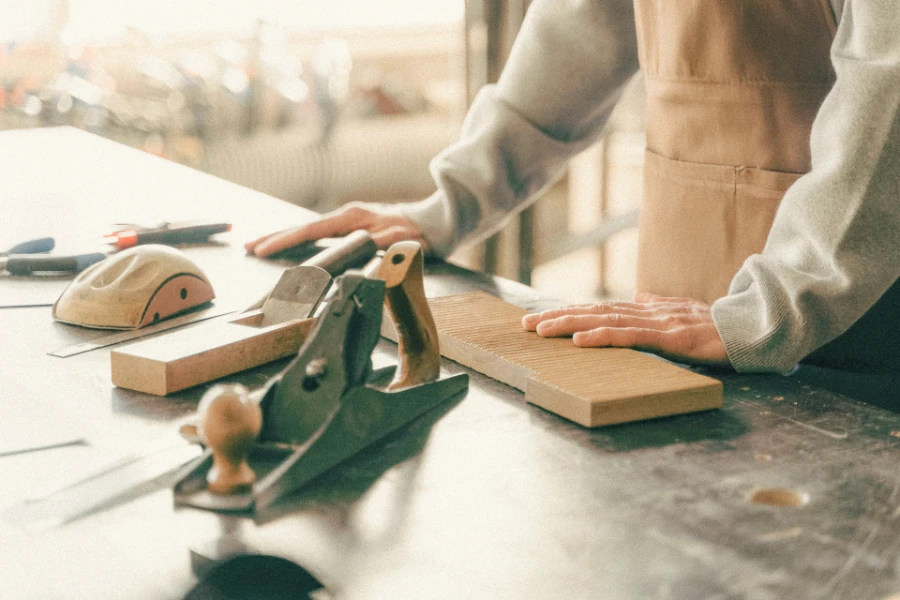Detalle de manos trabajando una tabla de madera con cepillo de carpintero sobre un banco de taller